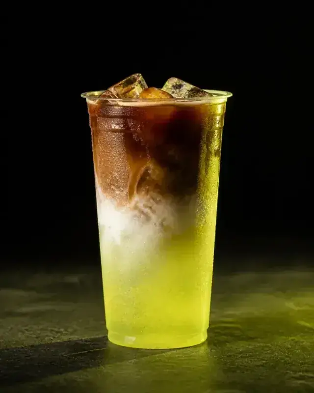 Layered dirty coffee and lime energy drink over ice in a clear cup